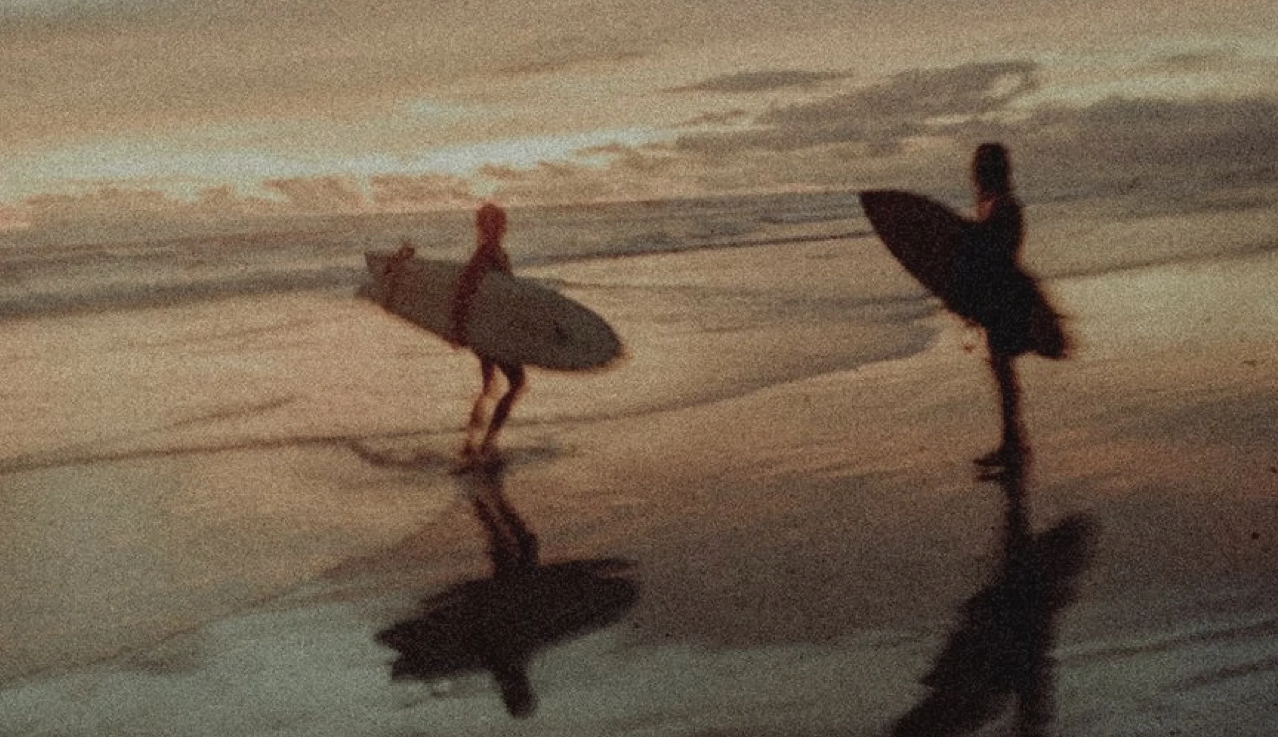 Two surfers walking the shoreline at sunset